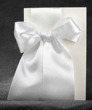 postcard white designer cardboard tabby with white satin bow wedding invitation on a dark cloth grey background
