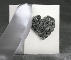 .greeting postcard with a convex image of the heart of a bouquet of gray roses white beige design cardboard with white satin bow wedding invitation on a light cloth grey background
