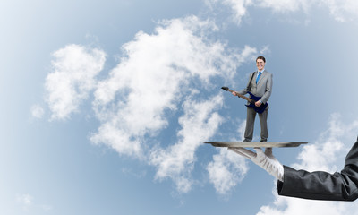 Businessman on metal tray playing electric guitar against blue sky background