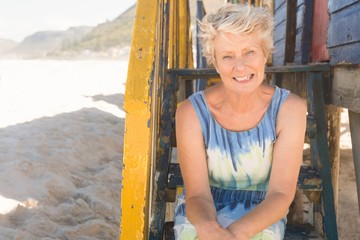 Obraz na płótnie Canvas Portrait of smiling senior woman sitting on steps of beach hut