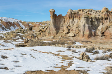 Fototapeta na wymiar Towering rock formations stand upright against the blue sky in the dry, arid, snow covered land of the Wyoming Badlands