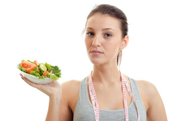 young beautiful girl with the measuring tape around the neck looks into the camera and holds high in vegetable salad plate close-up