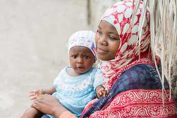 African black woman holding baby and sitting down outdoors 