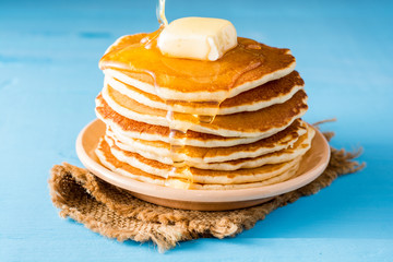 Pancakes with butter and honey on blue wooden table.