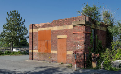 An abandoned and boarded up brick gate house near a factory