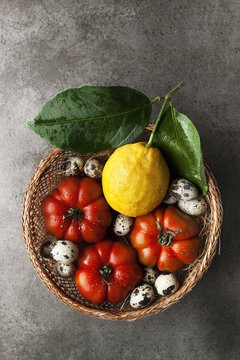 Organic products in a wicker basket. Fresh ripe tomatoes and quail eggs and lemon with leaves. healthy harvest