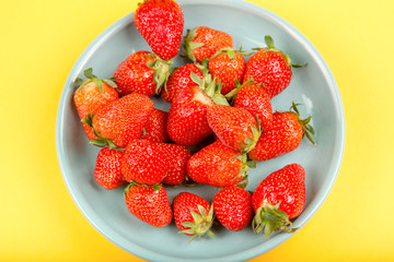 Fresh strawberry in a blue cup on a yellow background.