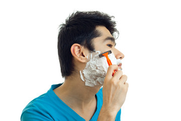 young guy with black hair stands sideways in front of the camera with the foam on the cheeks and shaves his beard close-up