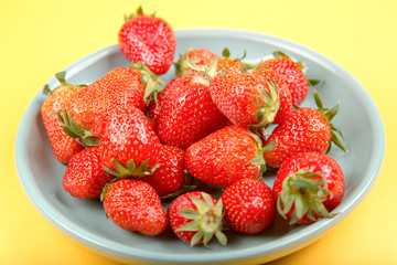 Fresh strawberry in a blue cup on a yellow background.