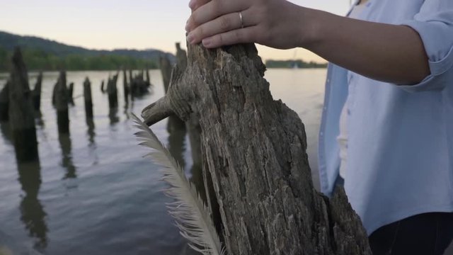 Woman Holds Onto Old Wood Pier, Camera Pans From Her Hand Up To Her Face, She Looks Out At View Of Water
