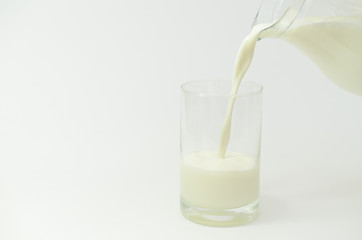 Milk in a jar on a light background is poured into a glass.
