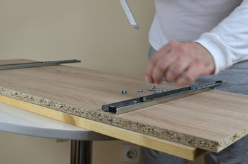 Man working - installing rails with a screwdriver on an element of a cabinet in his apartment