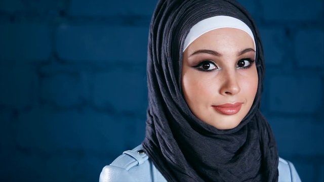 Close-up portrait of beautiful young Middle Eastern girl in black headscarf against brick wall background. Young Muslim woman looking shy and modest