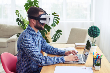 Man in VR glasses working with laptop sitting at table