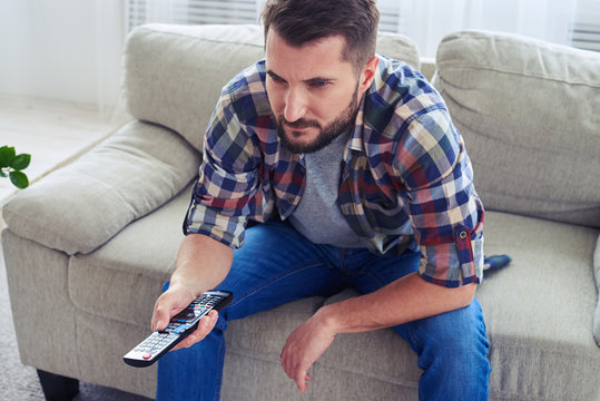 Brutal man watching attentively and switching channel with remote control