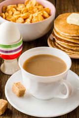 Breakfast table with coffee, boiled eggs, pancakes, cornflakes and milk.
