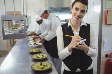 Smiling waitress with note pad in commercial kitchen