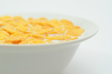 Cornflakes with milk on a spoon in a bowl on a light background.