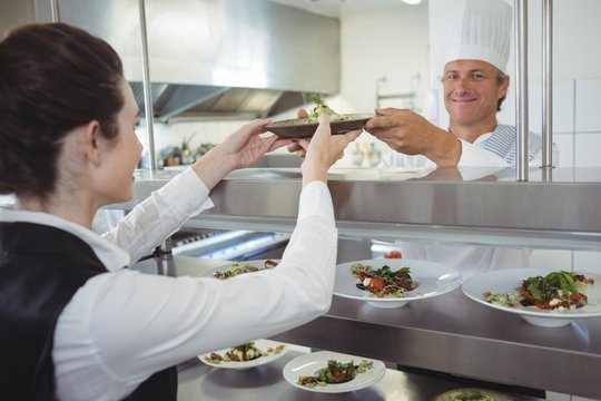 Chef handing food dish to waitress at order station
