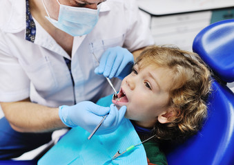 Male dentist examines the teeth of the patient cheerful child with curly red hair. Moloi boy smiling in dentist's chair. child mouth wide open in the dentist's chair