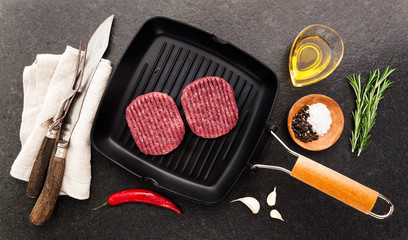 Raw hamburger cutlet in a frying pan for grilling. Burger. Cooking food. with cutting Cutlery for slicing and spices