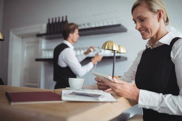 Smiling waitress using digital tablet at counter
