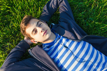 Young man listening music from smart phone on the grass in the park.