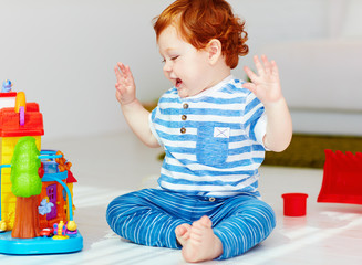 happy little redhead baby playing with toy house