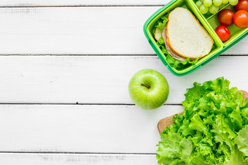 homemade lunch with apple, grape and sandwich in green lunchbox top view mockup