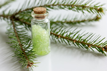cosmetic spruce salt in bottles with fur branches on white table background