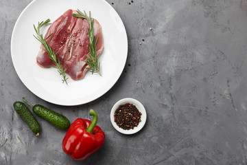 Raw duck breast in white plate with vegetables on gray stone background