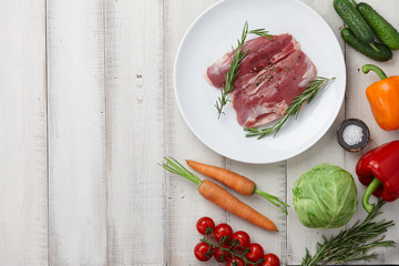 Raw duck breast in plate and fresh vegetables on white wooden background