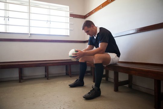 Serious player with rugby ball sitting in room - Powered by Adobe