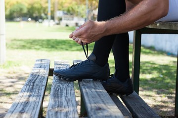 Low section of rugby player tying shoes on bench