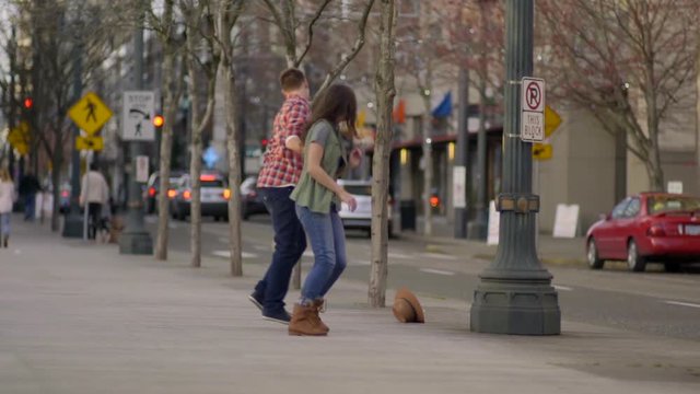 Cute Couple Run (Toward Camera) Woman's Hat Flies Off Her Head, Her Boyfriend Picks It Up, They Laugh And They Keep Running