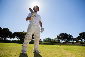 Confident player with cricket bat standing against sky © wavebreak3
