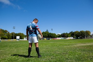 Rear view of rugby player holding ball at field - Powered by Adobe