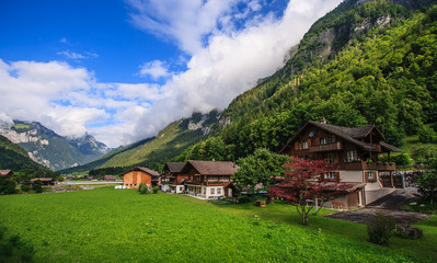 Fototapeta na wymiar Beautiful panoramic postcard view of picturesque rural mountain scenery in the Alps with traditional old alpine mountain chalets and fresh green meadow on a sunny day with blue sky and clouds