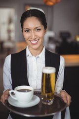 Portrait of waitress holding tray with coffee and beer glass