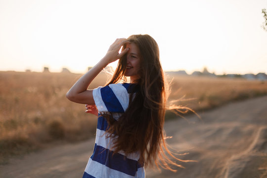 Silhouette of a young woman with long hair enjoying a beautiful sunrise in the dry field of lavender. Rear view of a romantic girl, windblown hair at sunset or sunrise.