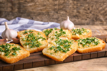 Tasty bread slices with garlic, cheese and herbs on wooden cutting board