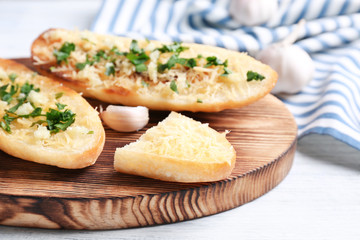Tasty bread slices with garlic, cheese and herbs on wooden cutting board