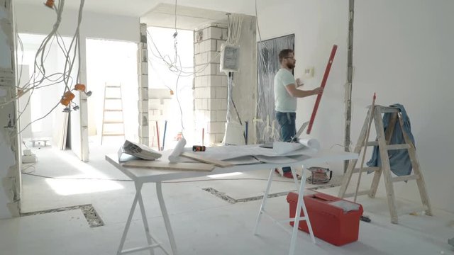 Male architect with blueprints checking wall with level at new home 
