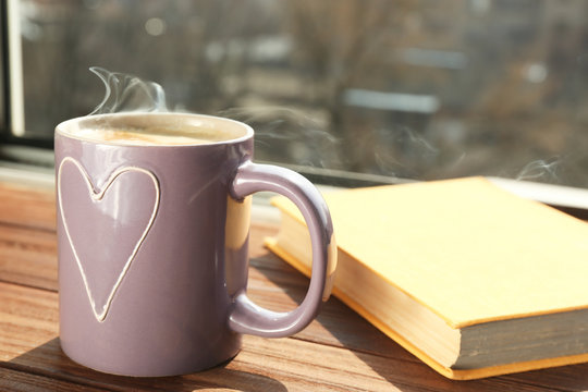 Cup with delicious coffee and book on window sill