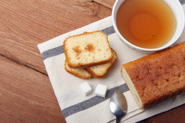 Black tea with sugar and cake with jam on a napkin and on a wooden background
