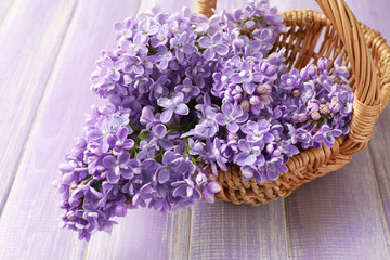 Wicker basket with beautiful bouquet of lilac flowers on wooden table