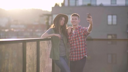 Cute Couple Have Fun Together Taking Silly Selfies On A Rooftop In A City At Sunset - Powered by Adobe