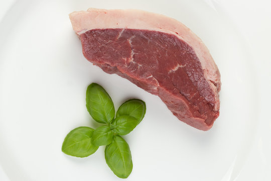  Slice of raw cow beef with some basil leaves isolated in white background - close up