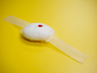 Close-up detail of a cotton ball and tape dressing with a blood stain on a yellow table. Healthcare...