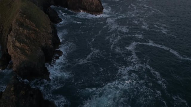 Flying over the sea and cliffs with waves breaking against the rocks, English coast, Perranporth Beach